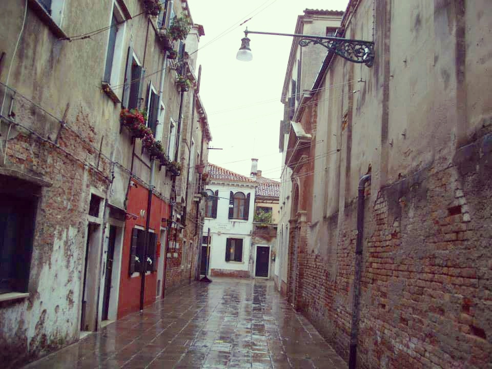 A small backstreet in Venice with tall buildings on either side in the rain