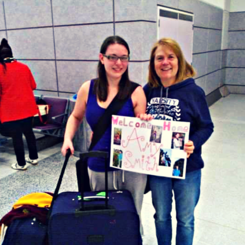 Myself and my mum in the airport as I arrived home from my study abroad experience in Sydney. Between us we are holding a sign saying welcome home Amy Smith