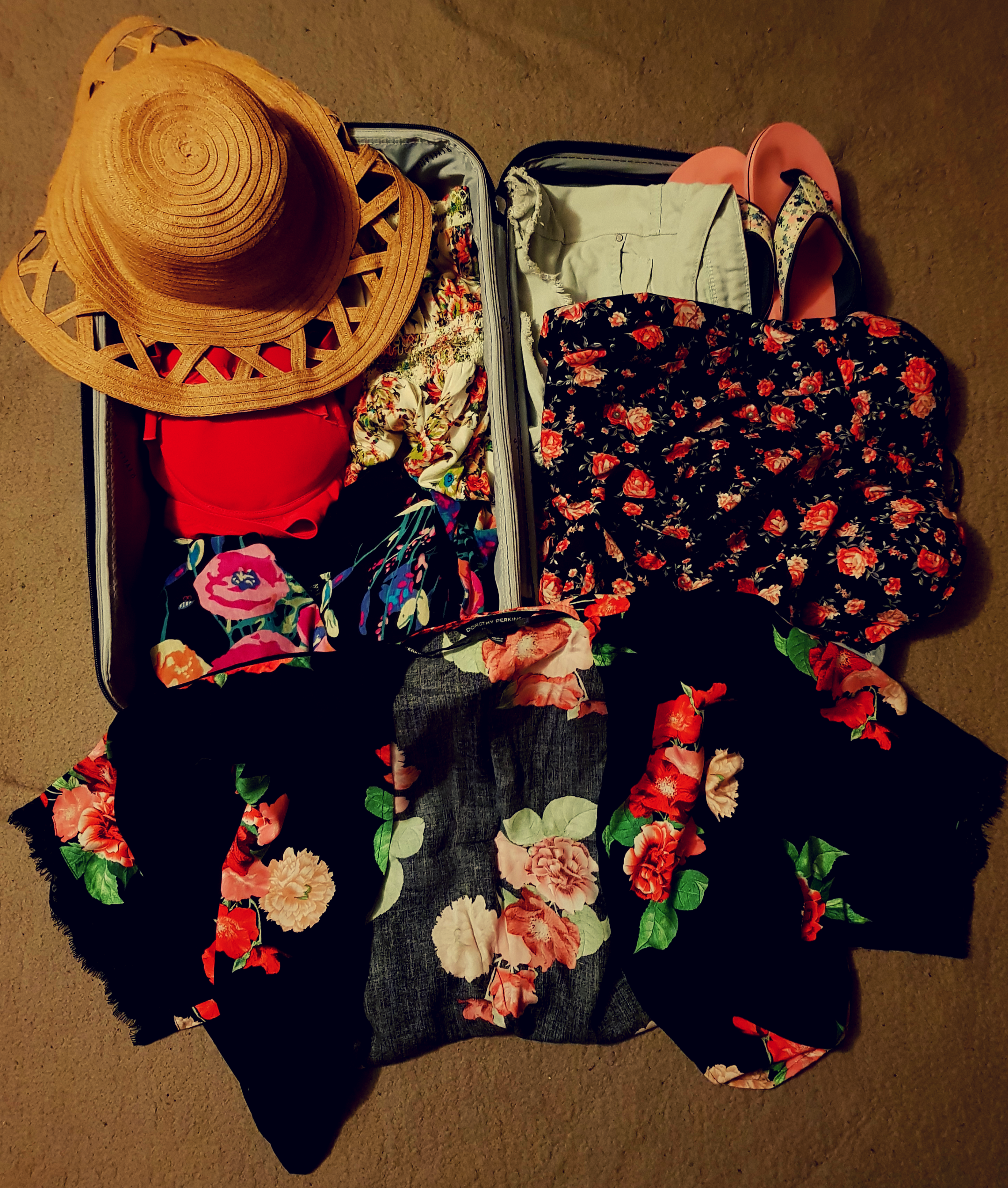 A purple suitcase with carry-on packing for Cyprus. A brown sunhat, red bikini, black and red dress, black and red kimono, white flowery dress, pink flip-flops and blue shorts.