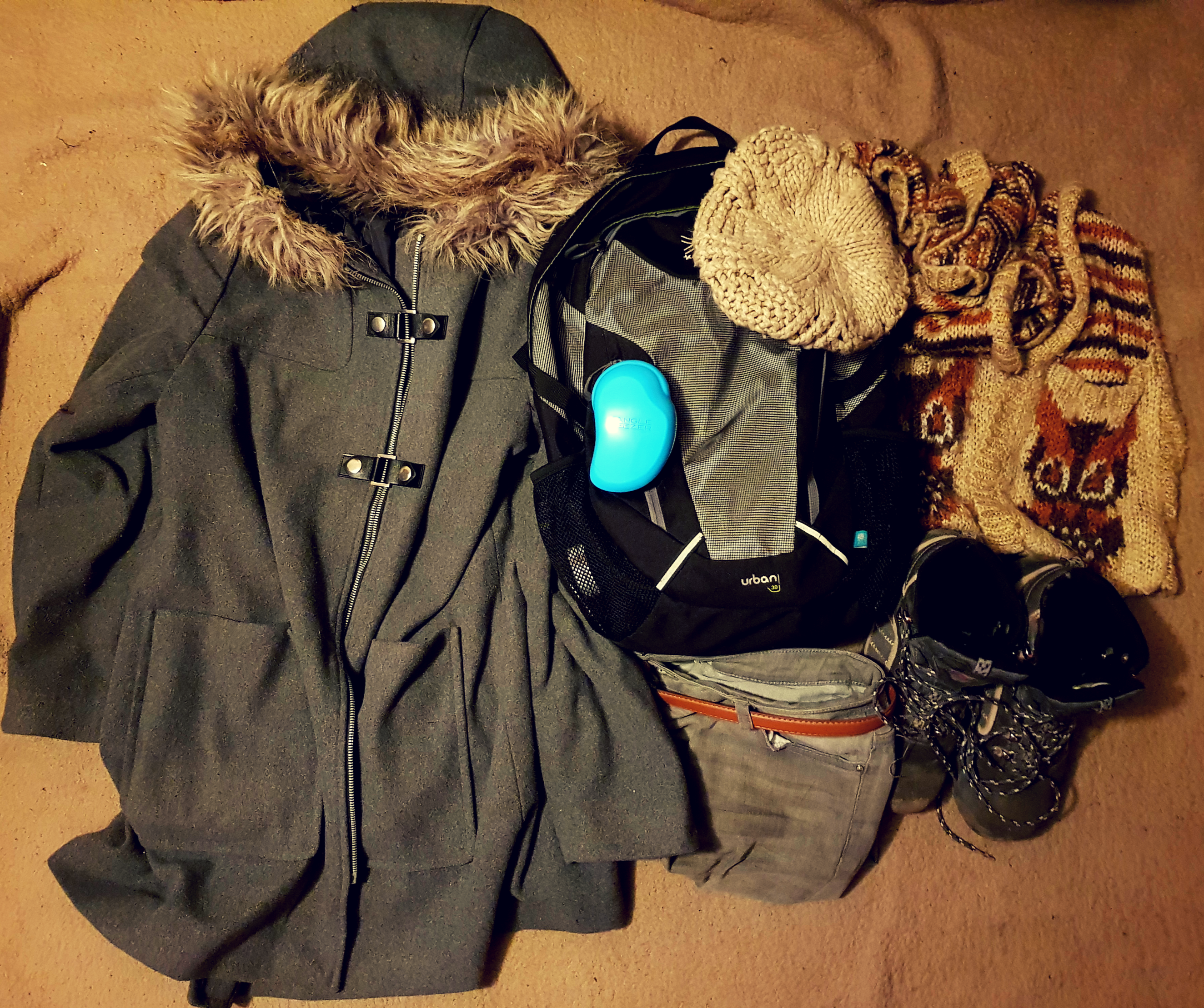 A black and grey back used for carry on luggage for 3 days in Brussels. A grey winter coat with brown fur around hood, brown wool hat and scarf, brown and grey hiking boots, grey jeans and a tangle teaser hair brush.