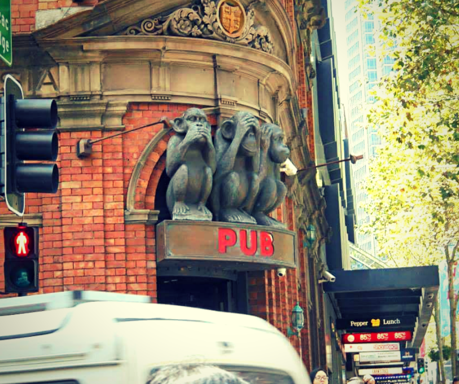 A red brick building with stone archway above a door. A plague says PUB in red and above this sits three stone monkeys, One covering its mouth with its hands, one covering its eyes with its hands and one covering its ears with its hands.