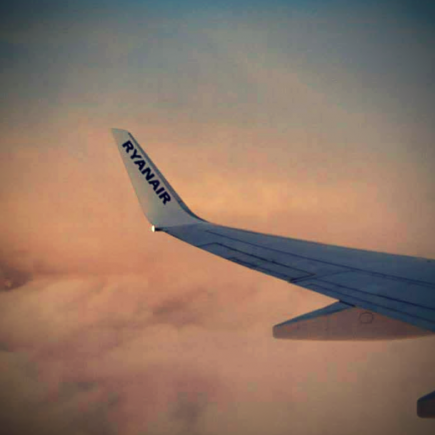 A Ryainair plane wing above the clouds at sunset taken through the airplane window.