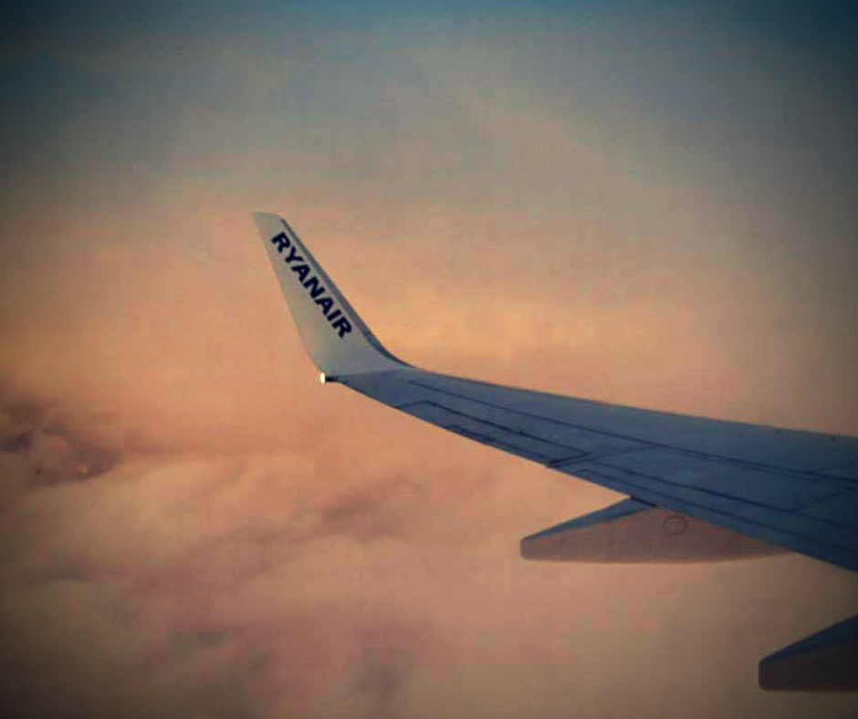 Countries in need: A Ryainair plane wing above the clouds at sunset taken through the airplane window.