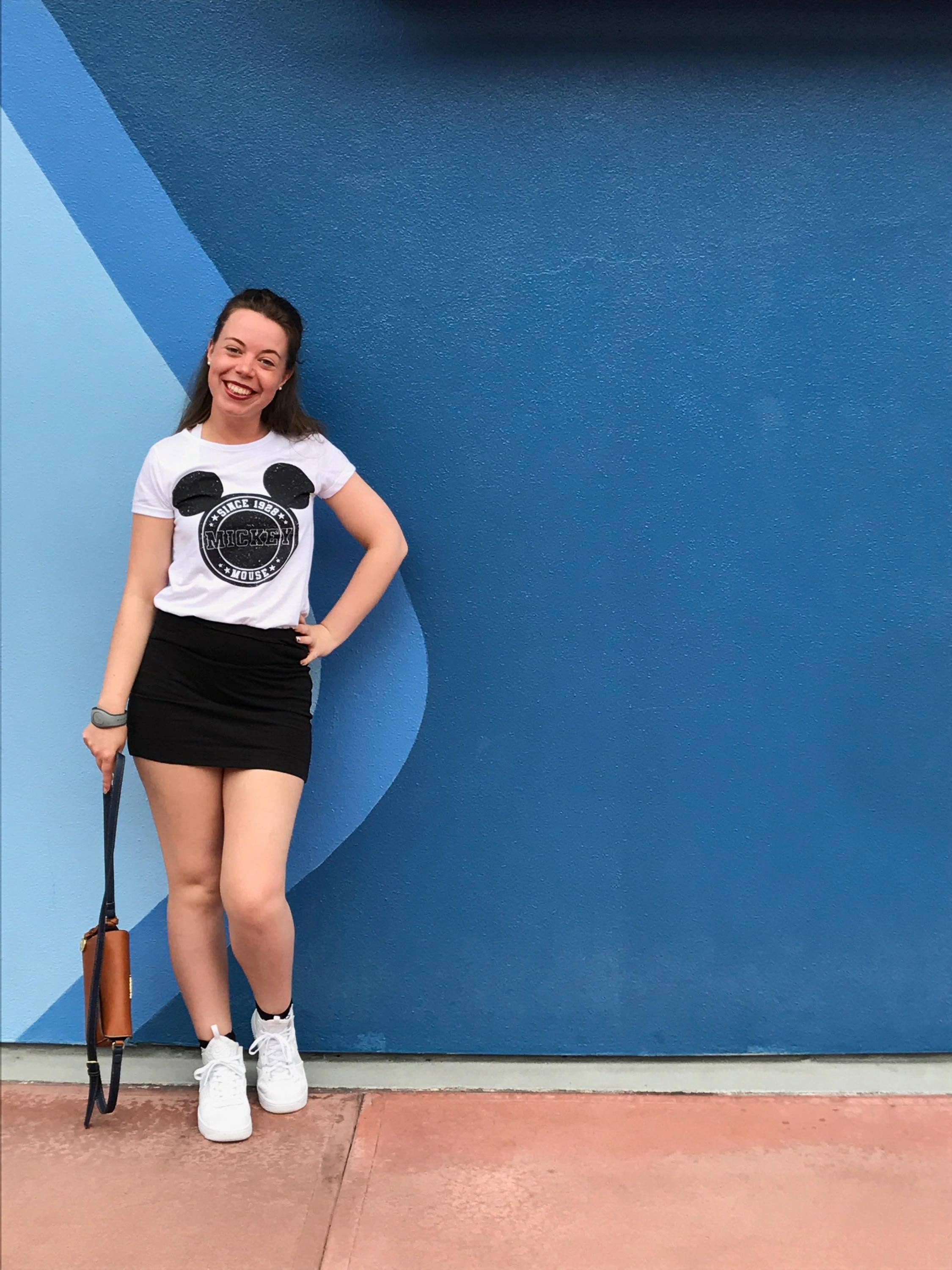 A girl with Mickey mouse t-shirt and black skirt in front of a blue wave patterned wall