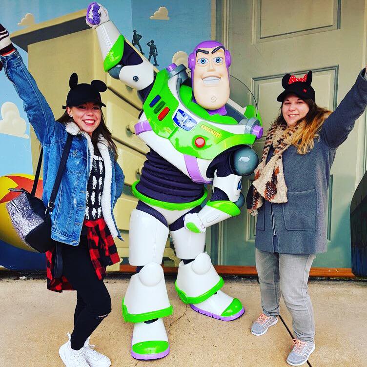 2 girls wearing Mickey ear hats posing with their arms in the air with Buzz Lightyear at his Character meet and greets