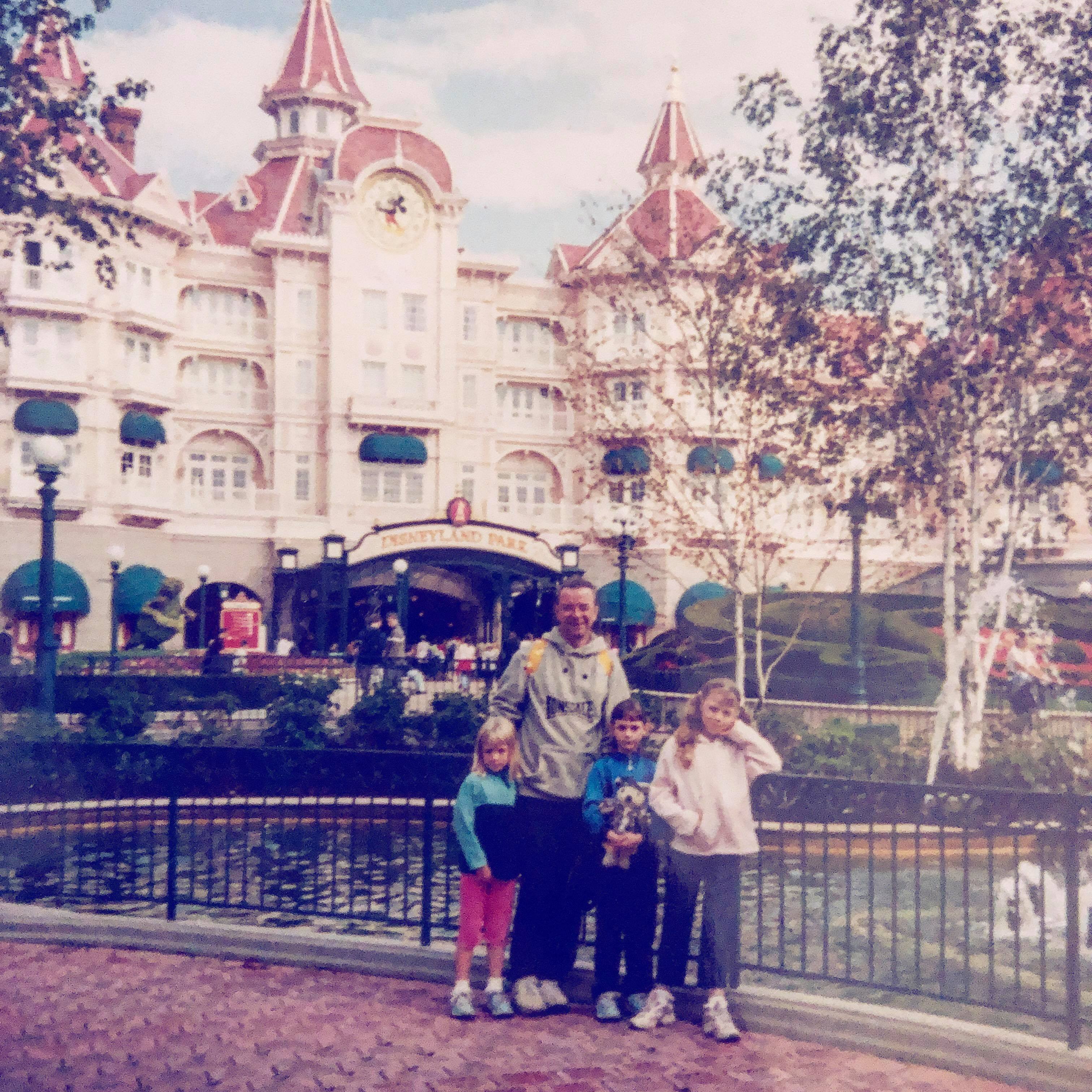 Old family photo of 3 young girls and their dad at Disneyland Paris in front of the Disneyland Hotel