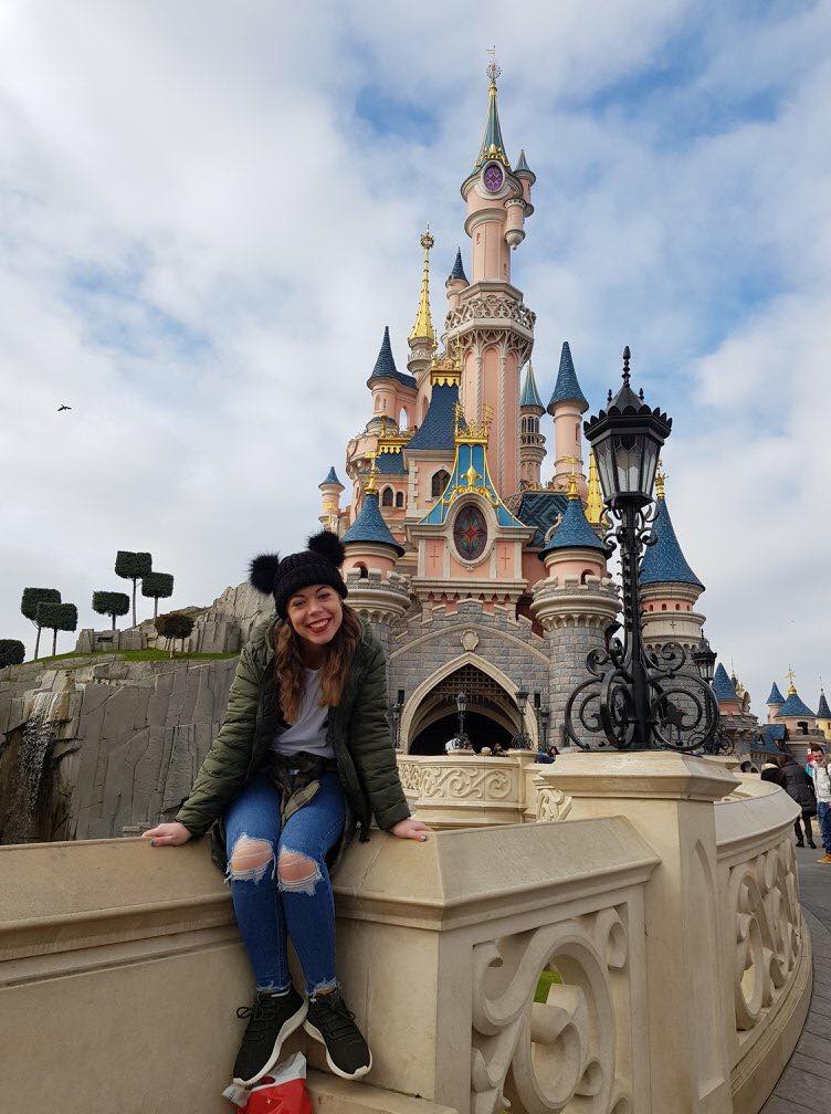 A girl with Mickey mouse hat sat on the wall in front of the pink sleeping Beauty's castle at Disneyland Paris