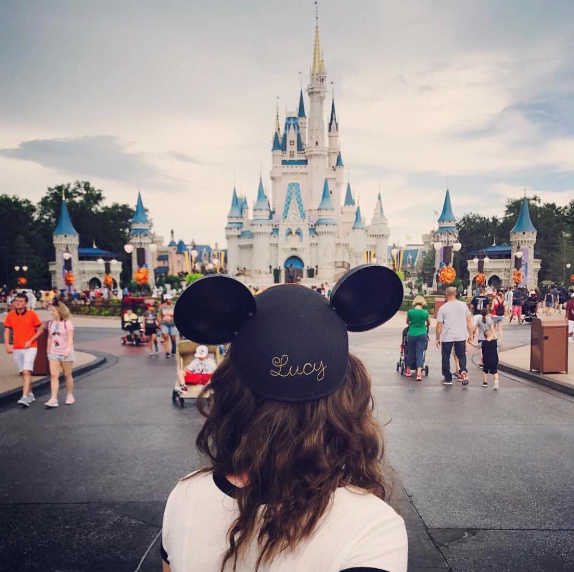 A girl with Mickey hat with Lucy written on it standing in front of the grey Cinderella Castle at Disney World