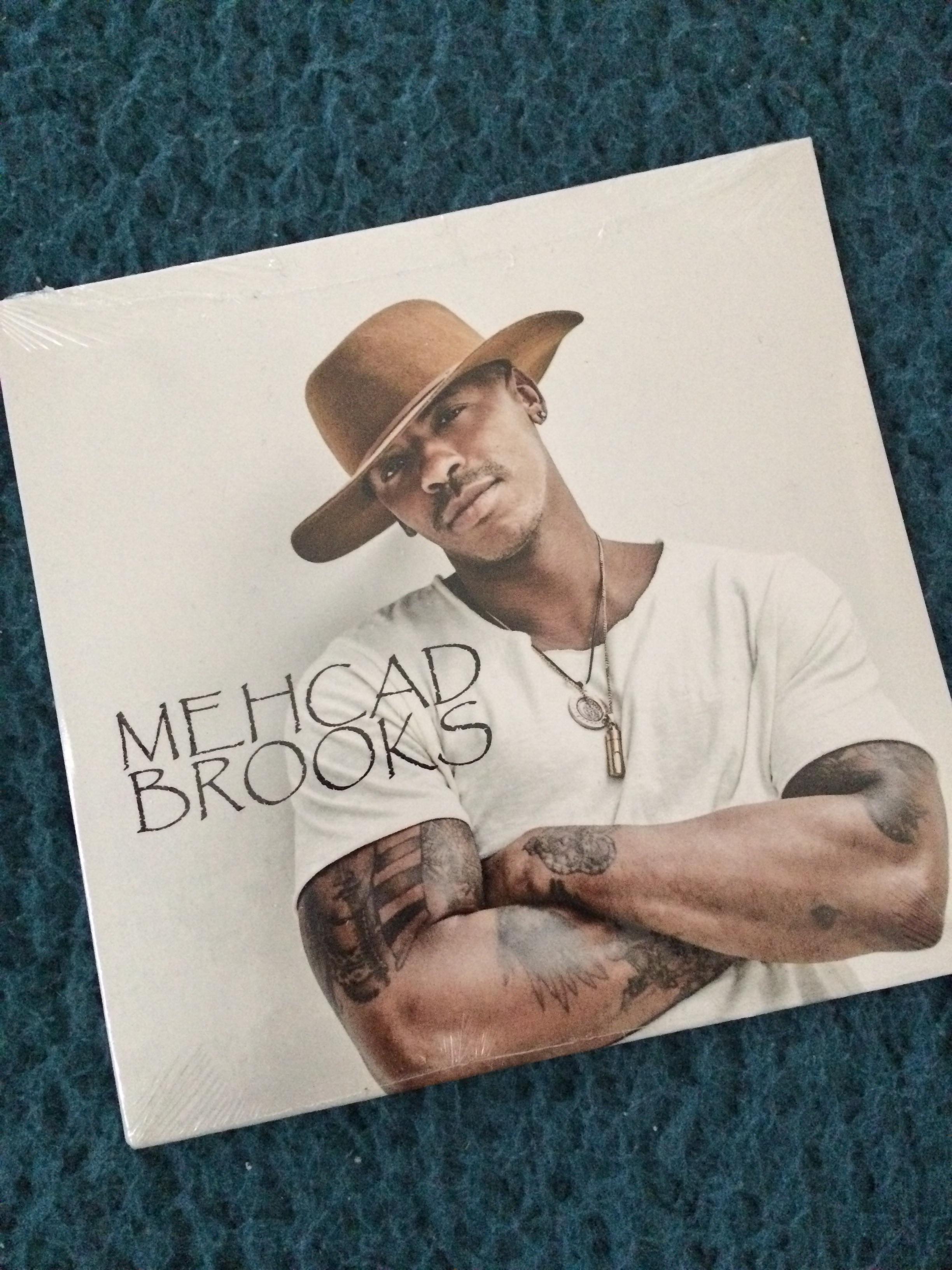 Photo of the cover of Mehcad Brooks demo album. He stands with his arms crossed in a white t-shirt and brown hat on a white background with Mehcad Brooks written over. This album was recieved from him at the Heroes and Villians Fan Fest London.