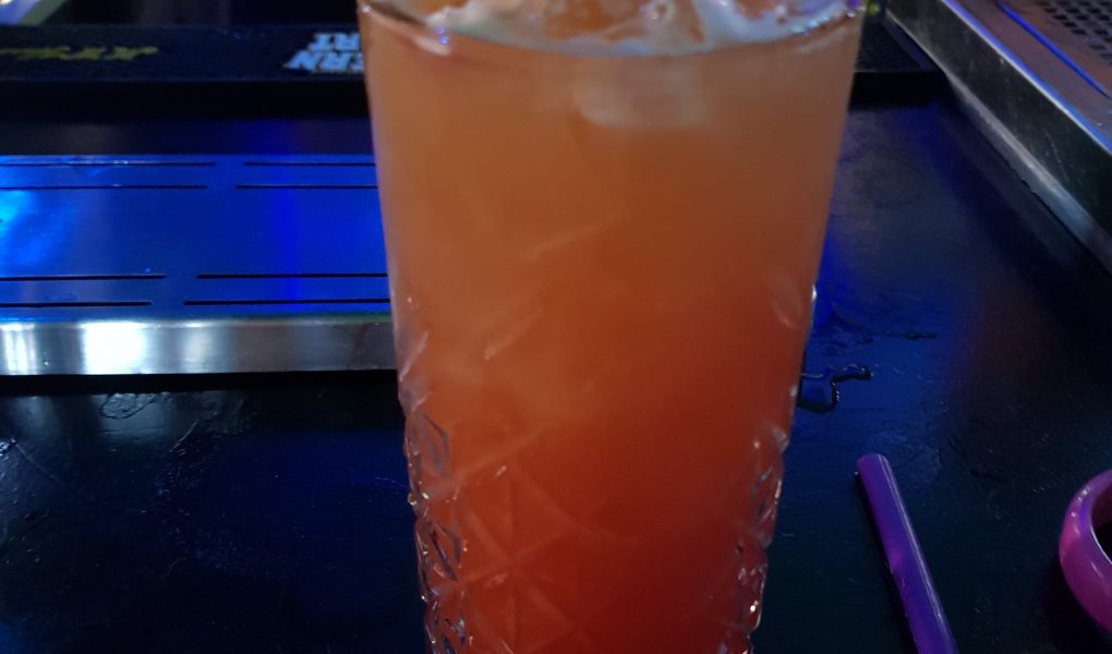 Orange and Red drink in a tall glass with ice and a pineapple slice served in the bar at Andwhynot Mansfield