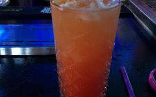 Orange and Red drink in a tall glass with ice and a pineapple slice served in the bar at Andwhynot Mansfield