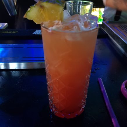 Orange and Red drink in a tall glass with ice and a pineapple slice served in the bar at Andwhynot Mansfield