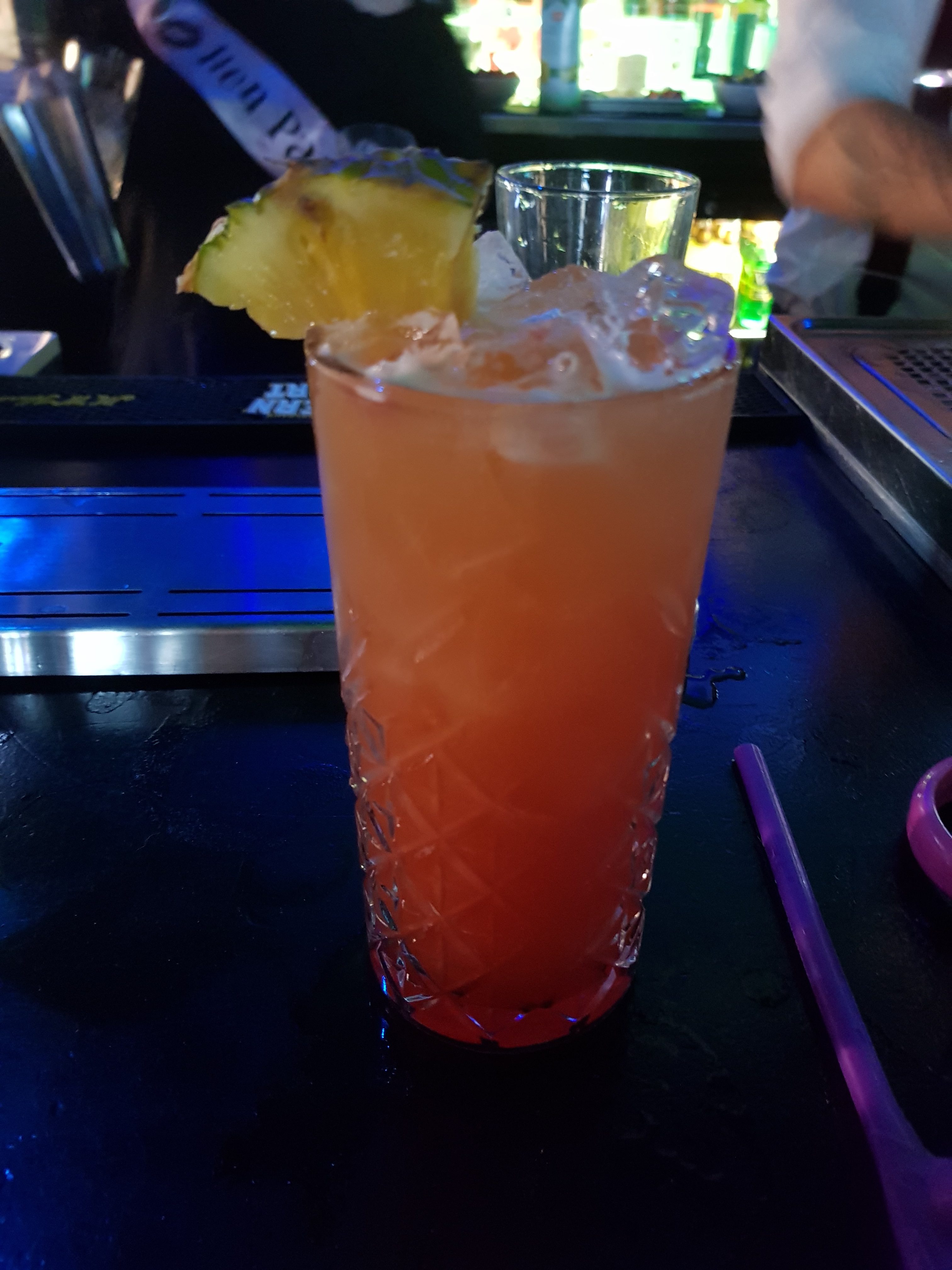 Orange and Red drink in a tall glass with ice and a pineapple slice served in the bar at Andwhynot Mansfield