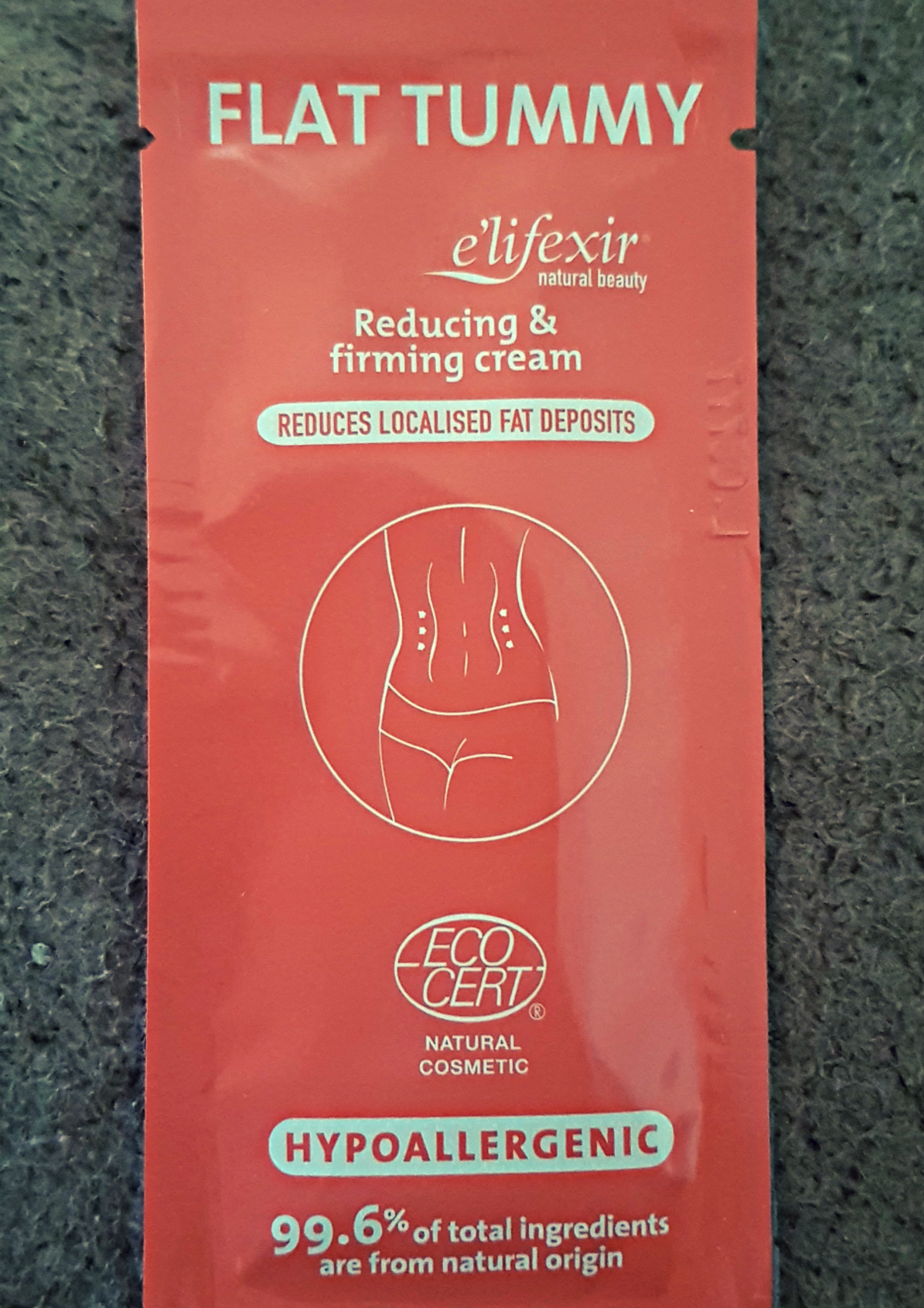 Red sachet with E'lifexir flat tummy cream written and a diagram of a slim tummy