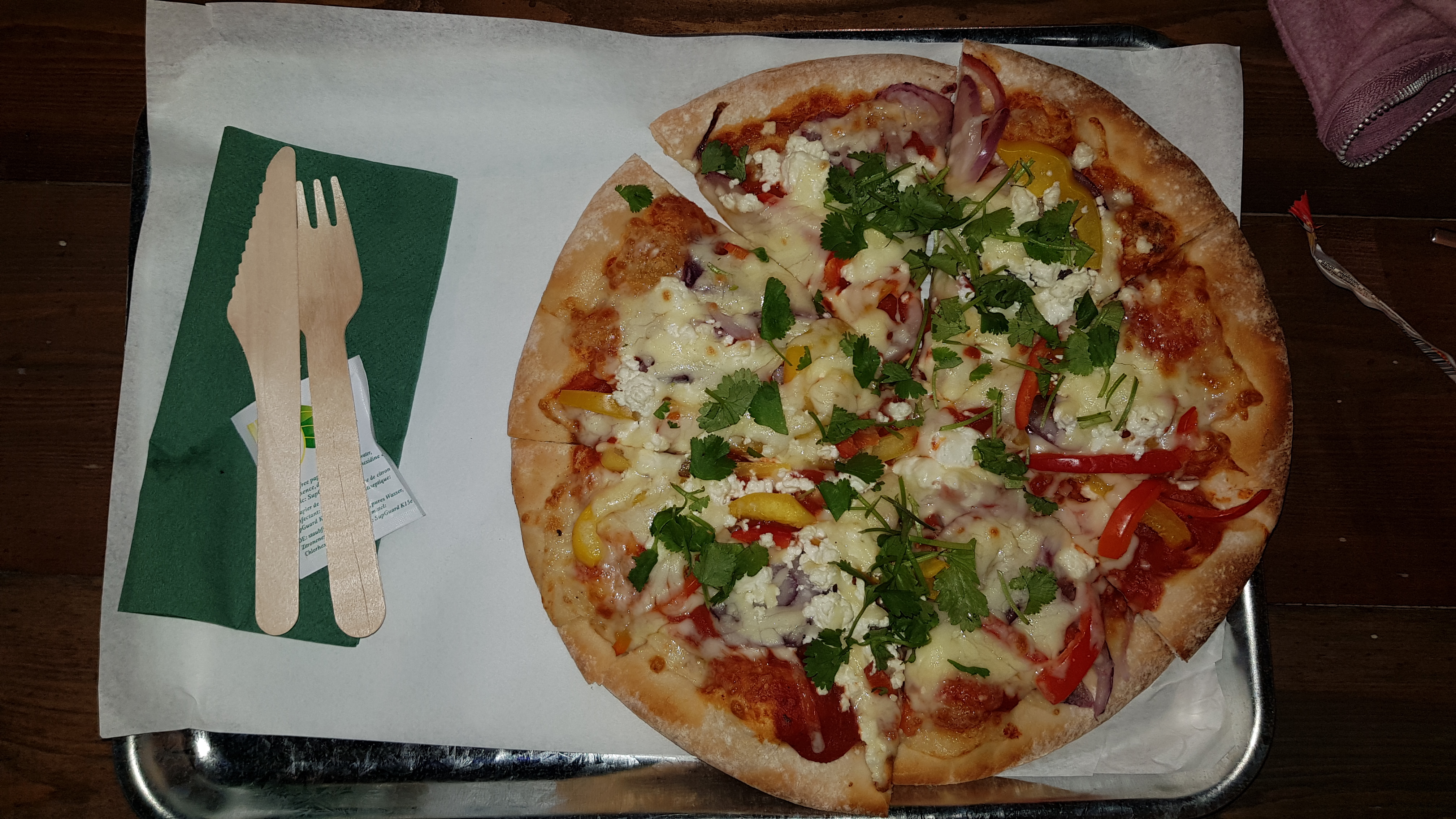 Vegetarian Pizza served in a silver tray with wooden knife and fork. The pizza has onion, peppers, cheese and herbs on it.