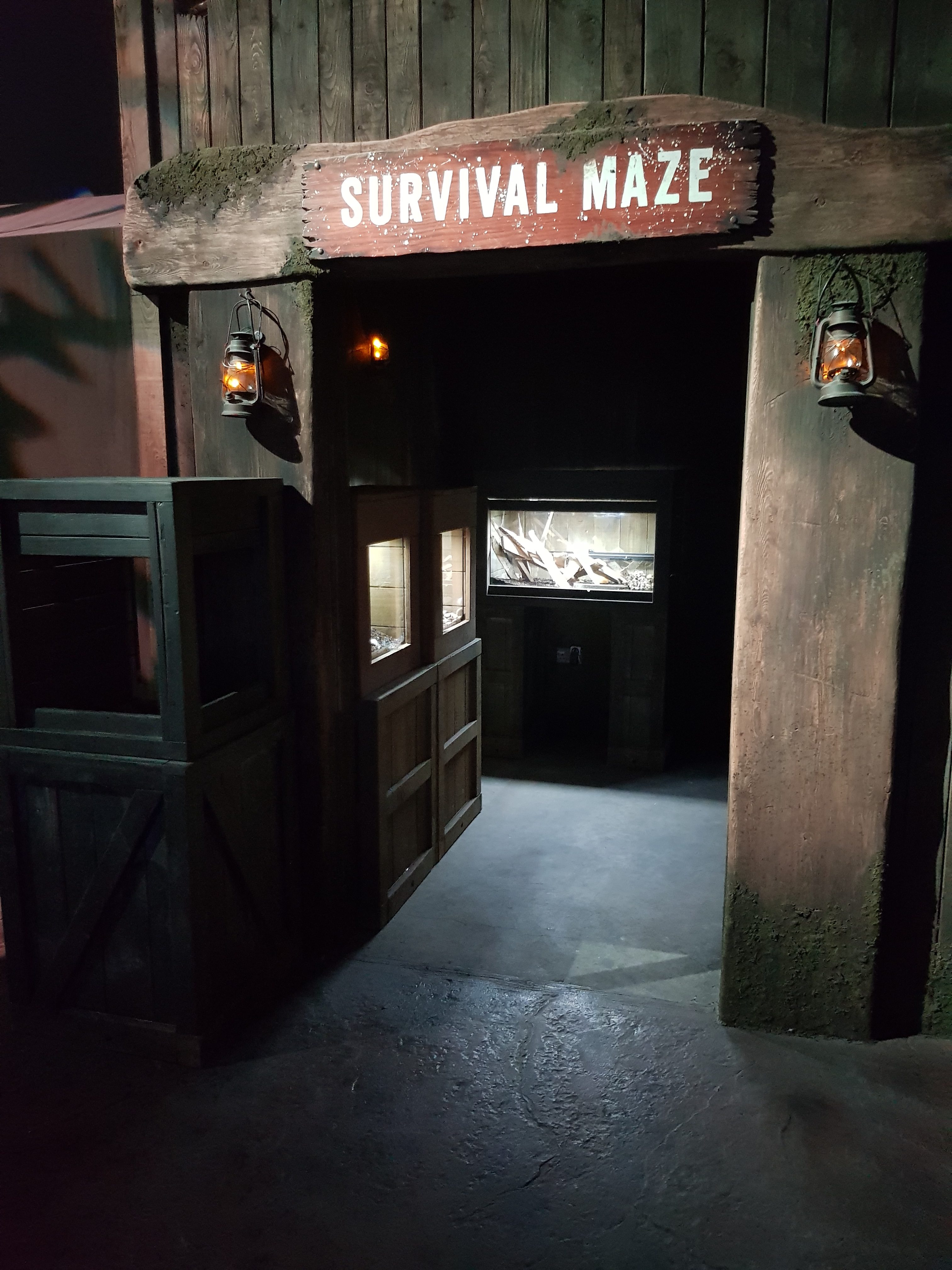 The Bear Grylls Adventure. Adrenaline Rush Activities. Survival Maze. A wooden door frame with SURVIVAL MAZE written above in white. On the door posts are old fashioned mining lanterns and through the door way you can see animal tanks.