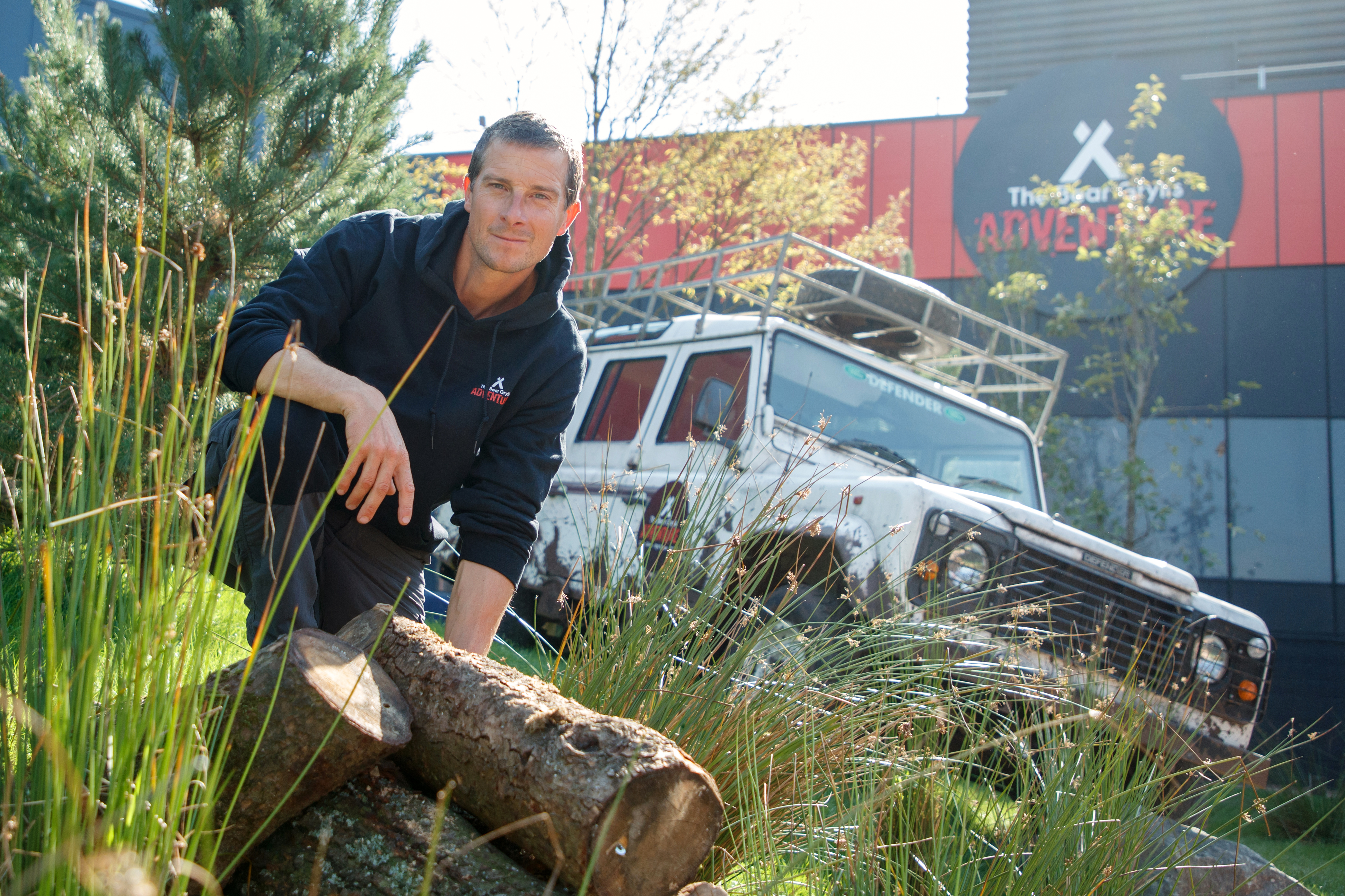 The Bear Grylls Adventure. Bear Grylls knelt outside the new site with a white jeep behind him