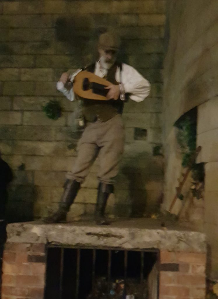 Gary, an elderly gentleman, dressed in old fashioned clothing and holding a wooden instrument with buttons and a crank