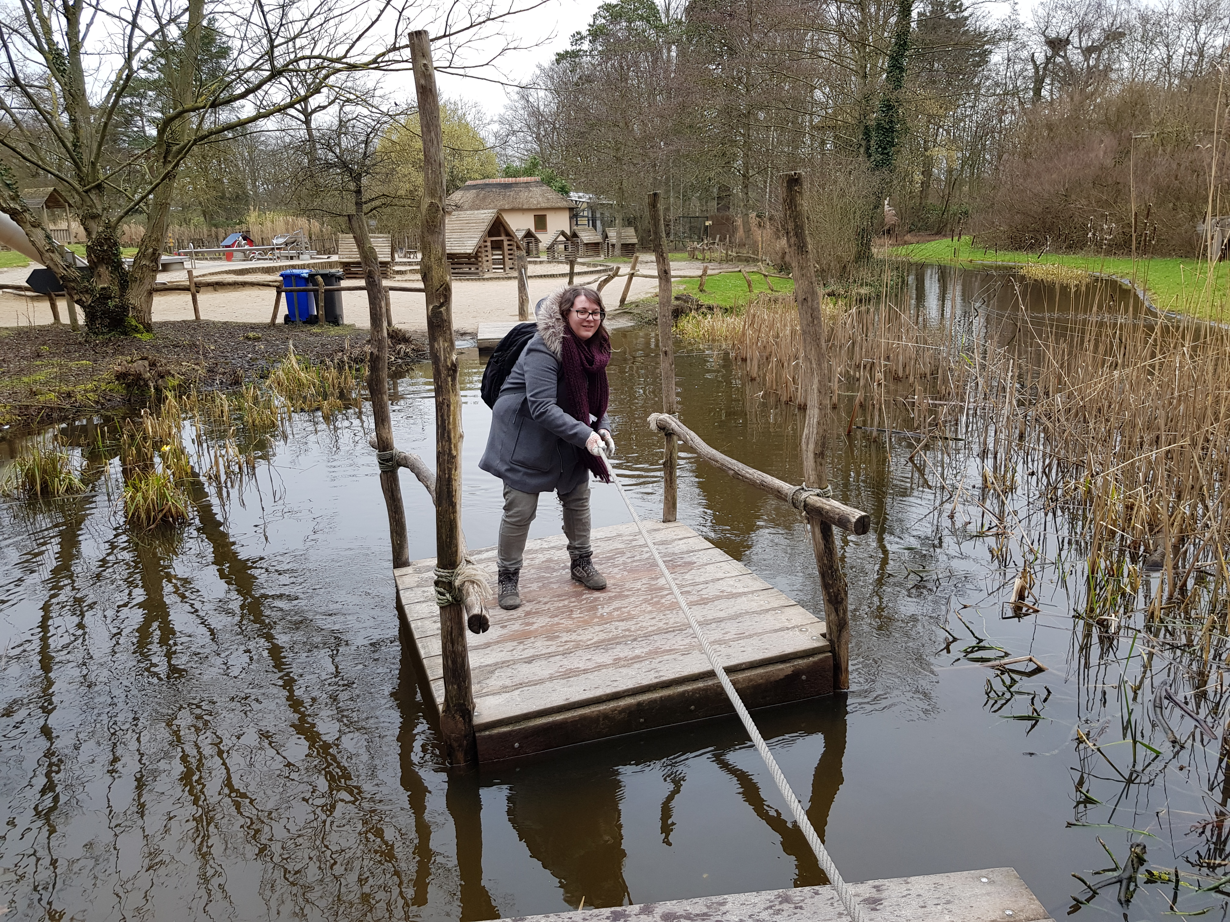 A girl pulling herself across a lake using a wooden raft and a rope