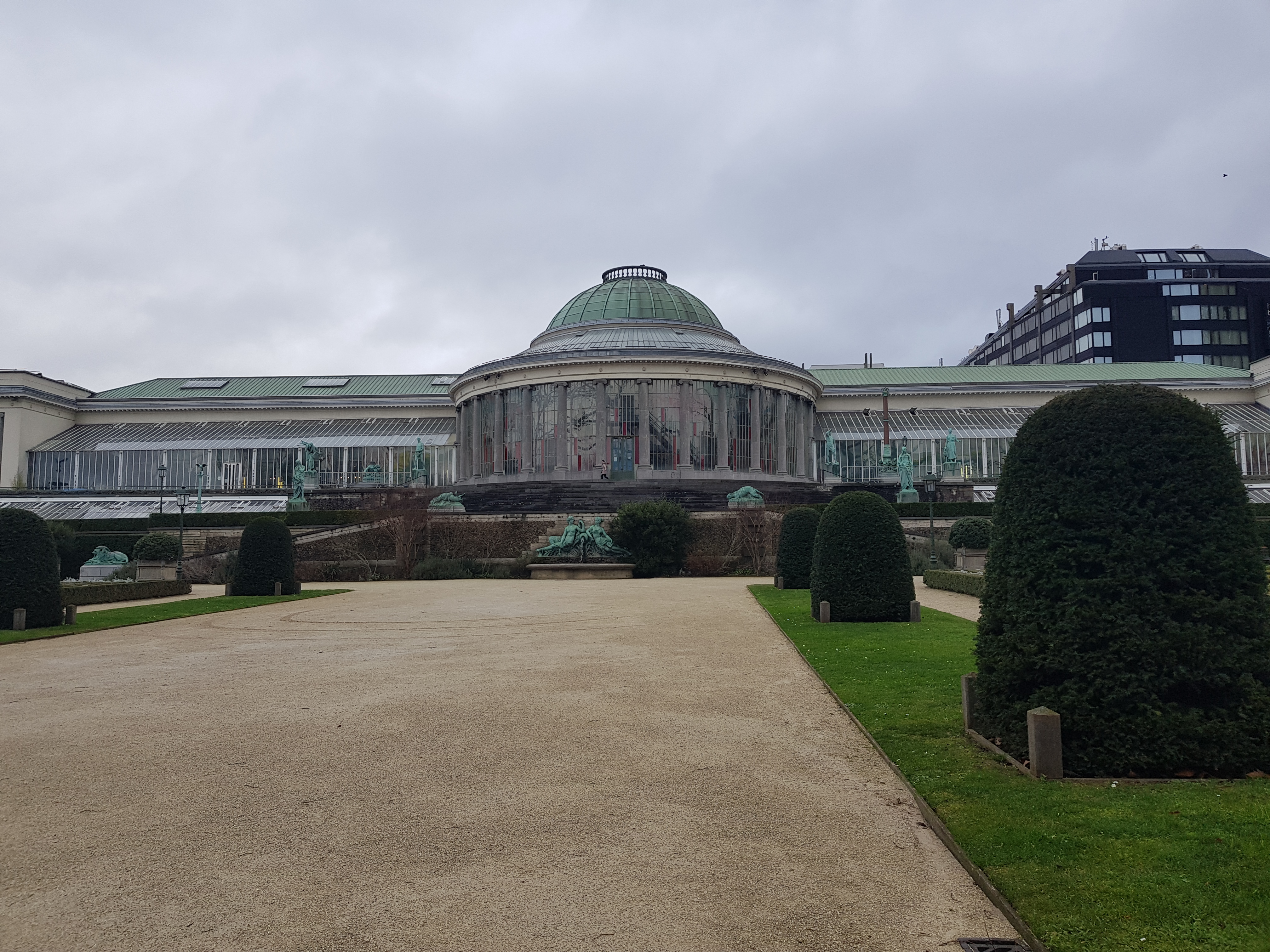 a large greenhouse with shaped bushes in a line coming away from it