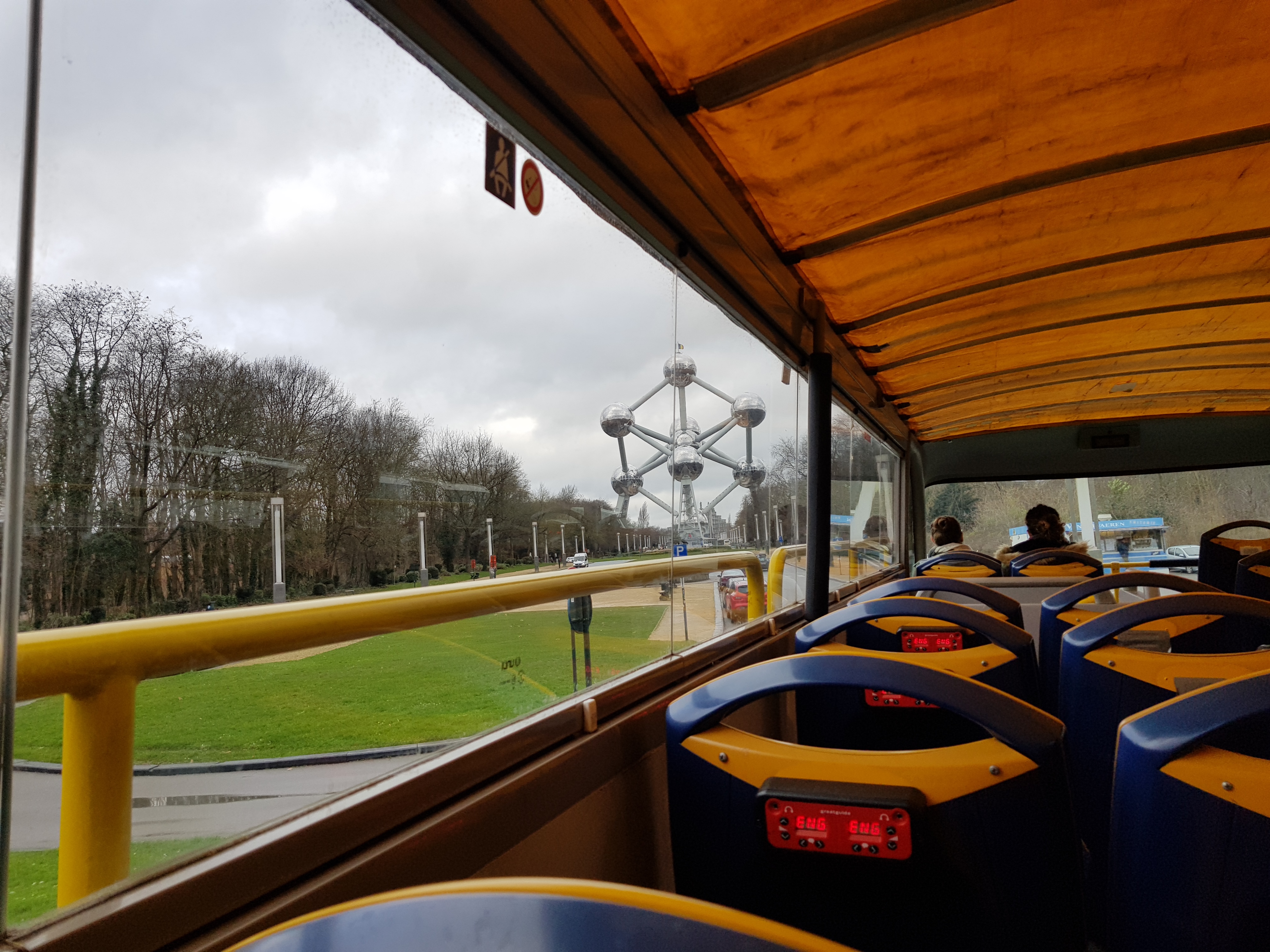 Inside of a double decker sightseeing bus with a view of the Atomium from the side. The Atomium is a large metal sculpture in the shape of an atom