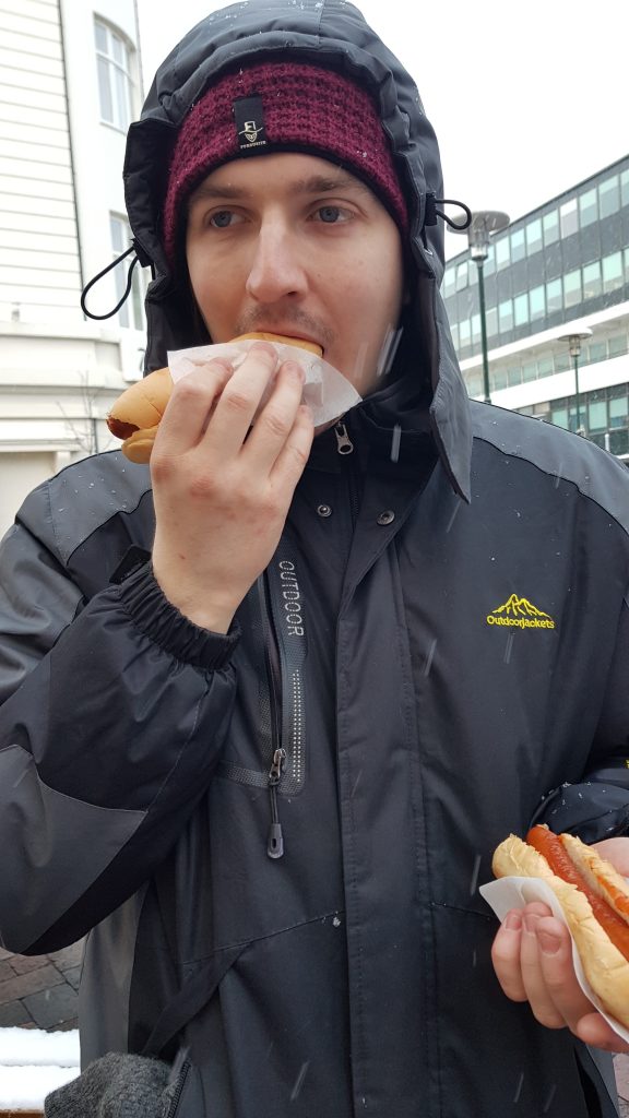 A guy eating one hot dog while holding another in his other hand