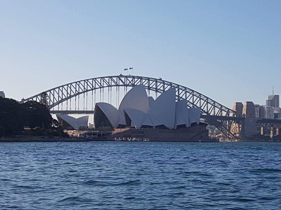 A view of the Sydney Harbour with the Sydney opera house in front of the harbour bridge