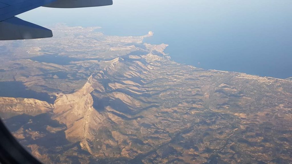 A view outside of an aeroplane window with a view of the ocean and a mountain range