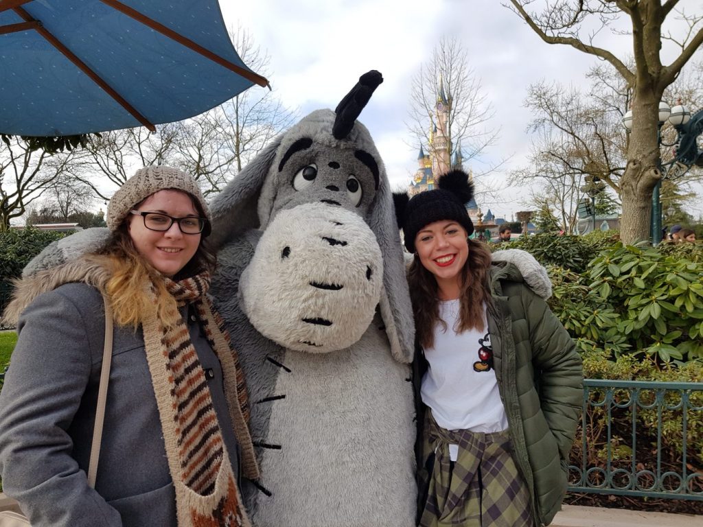 two young girls standing with arms round Eeyore character meet