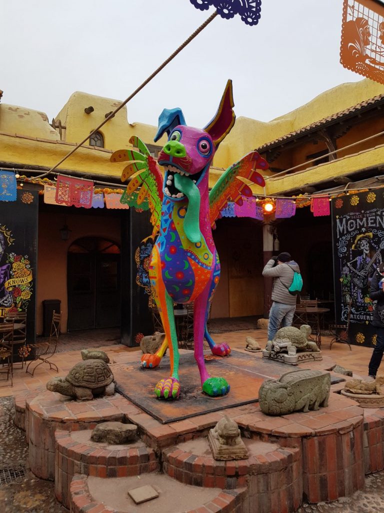 Statue of a multicoloured dog with wings (Dante from the Disney film Coco) standing in the courtyard of Fuente del Oro a Mexican restaurant in Disneyland Paris.