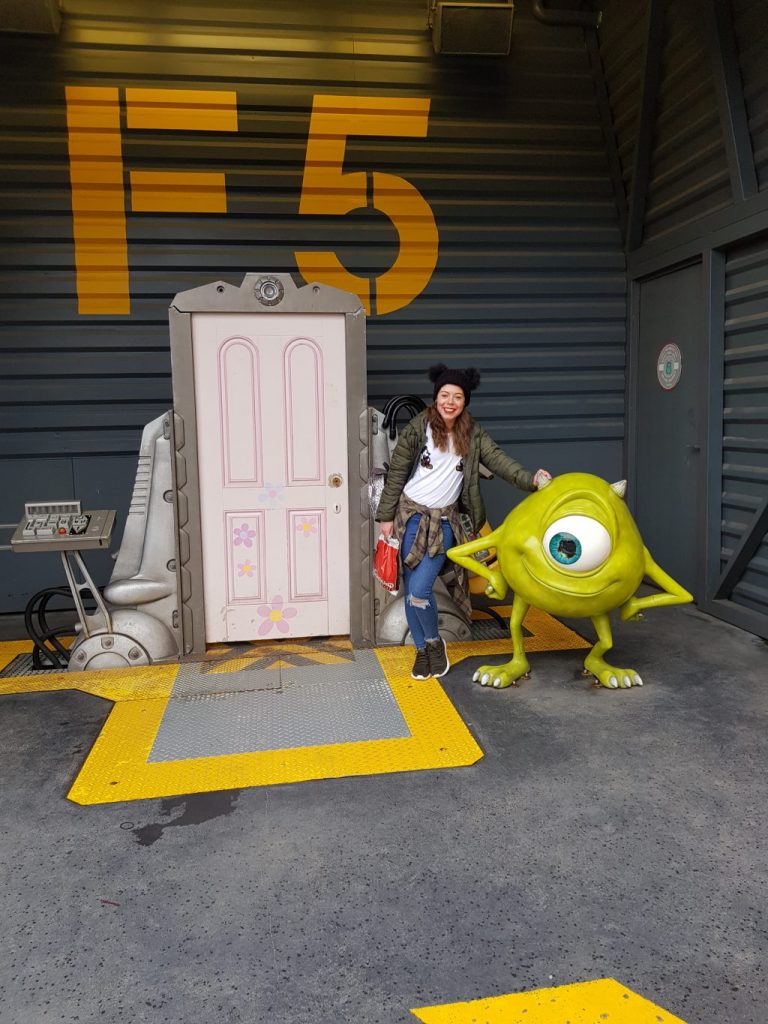 a white door from monsters inc with a small green monster (Mike Wazowski) and a girl in between 