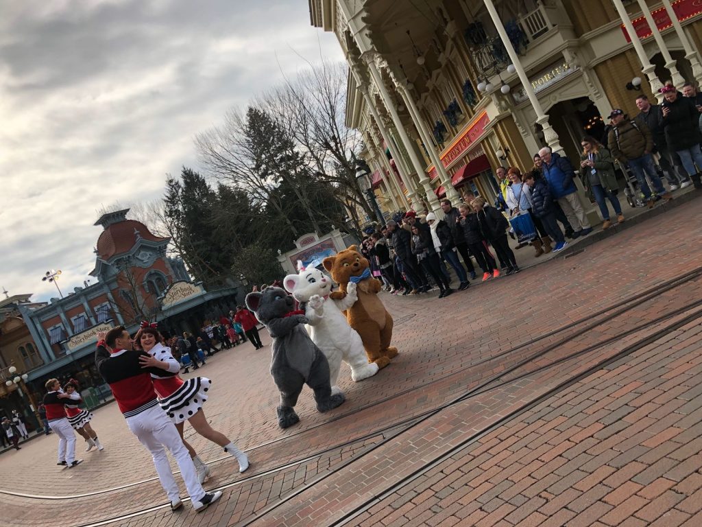 Aristocat kitten characters walking down Mainstreet USA together while dancers dance around them on the guest star parade