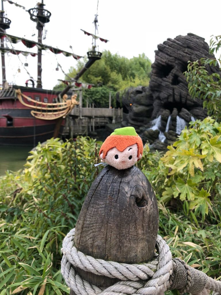 Peter Pan Tsum Tsum on a wooden post in front of a red pirate ship and Skull rock