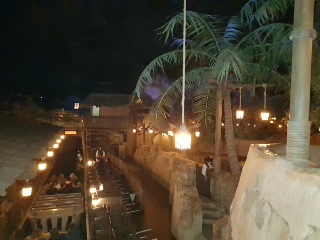 Inside the Pirates of the Caribbean ride at the loading dock. This is one of the best Disneyland Paris rides for adults. A water way goes through the building with large wooden boat style carriages with lanterns. Stone walls line the waterway and on the other side of the wall are palm trees and hanging lanterns