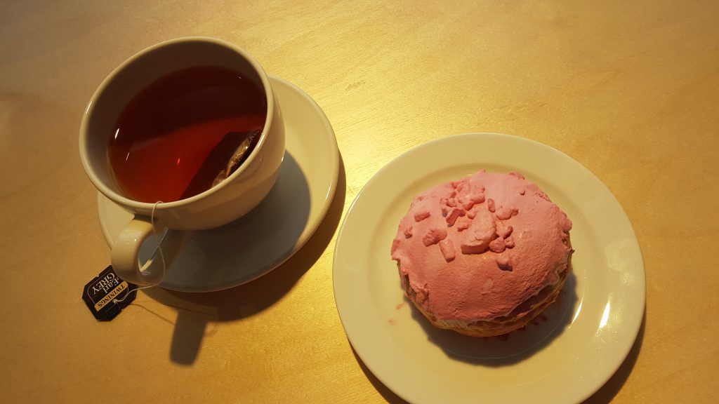 A cup of Earl Grey tea next to a pink lemon meringue donut in the Primarket Cafe