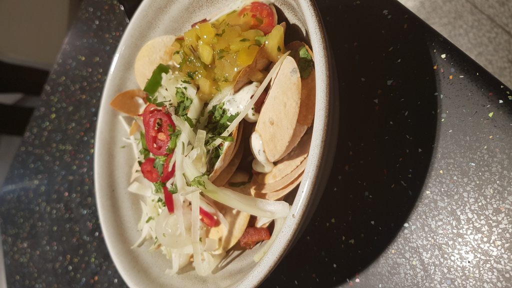 Popadoms covered in Chicken Tikka and salad vegetables in a bowl.