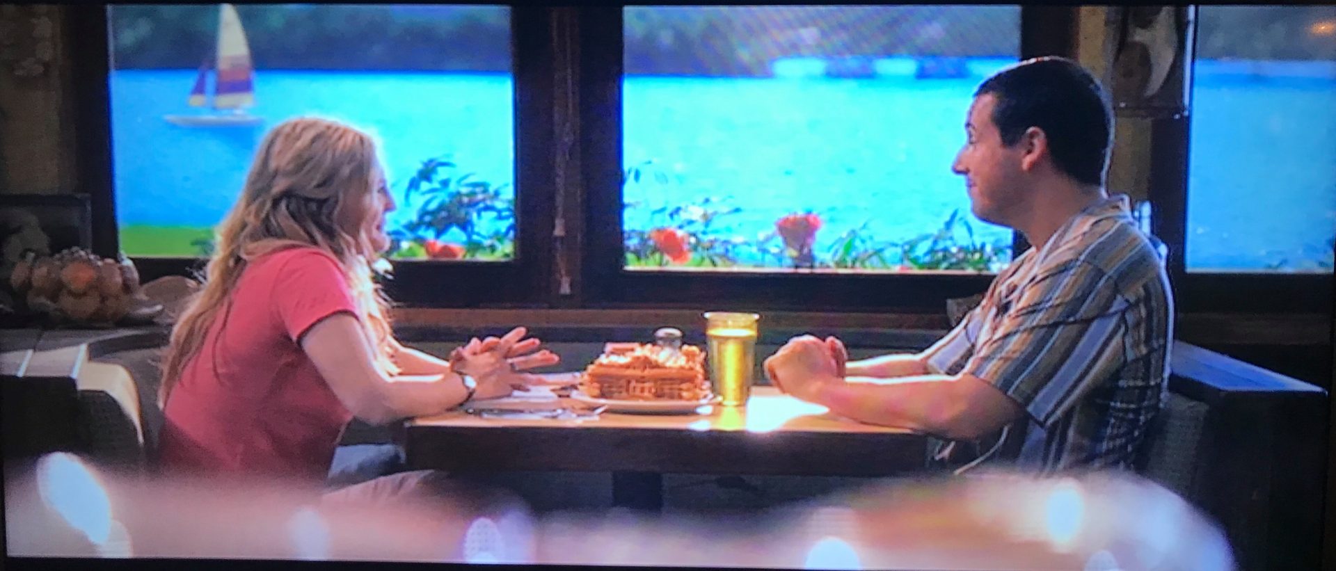 A scene from 50 first dates where a man and woman are sat in a restaurant across the table from each other with a large fishtank in the background