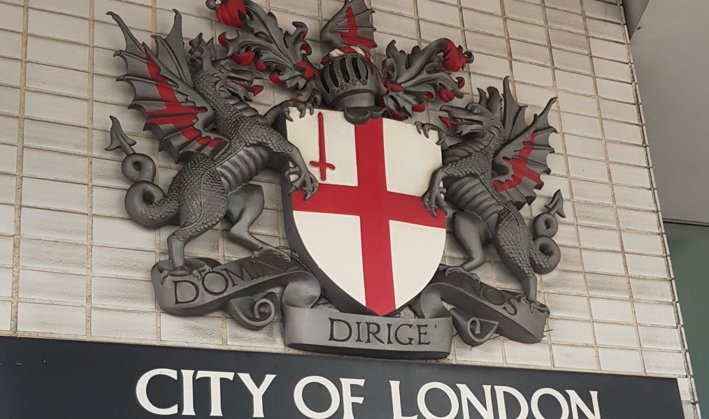 Sign saying City of London with an English flag on a shield being held by two dragons. One of the clues in Hidden City London
