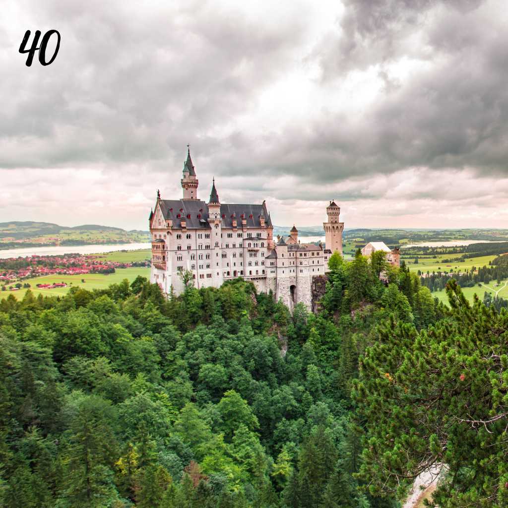 Number 40. Bran Castle white castle with grey roof on top of a hill surrounded by trees.